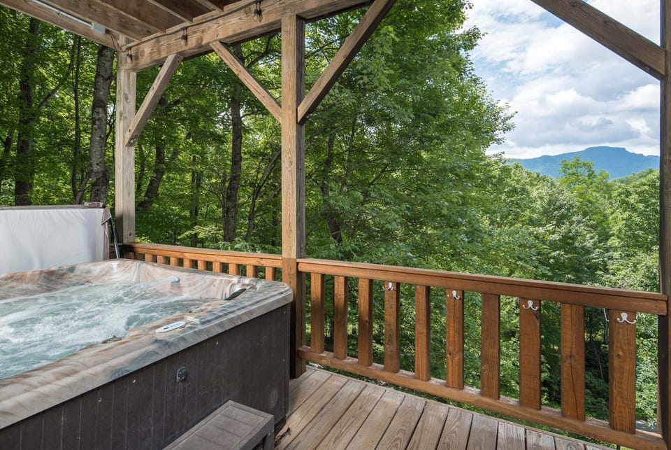 Relax in the private hot tub on the covered deck with peaceful forest scenery and Grandfather Mountain views