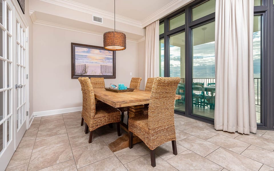This dining area features a rustic wooden table with woven chairs, with stunning beachfront views through large windows