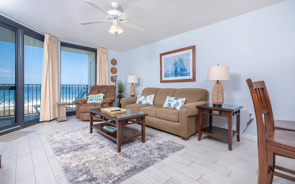 Living area features a comfortable sofa with queen sleeper, accent chairs, and a vibrant gulf front view from the balcony