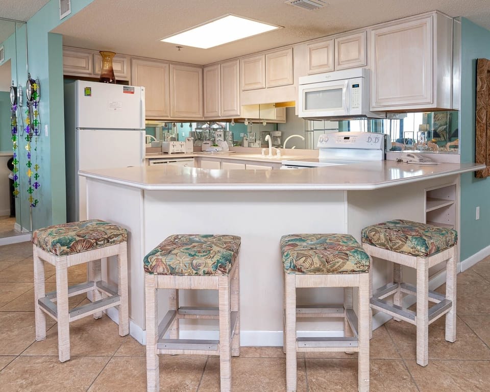 Kitchen area features light cabinetry, a breakfast bar with four cushioned stools, and modern appliances for convenience