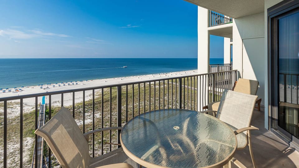 Balcony with a glass table and chairs offers a serene view of the beach and gulf, perfect for relaxing moments