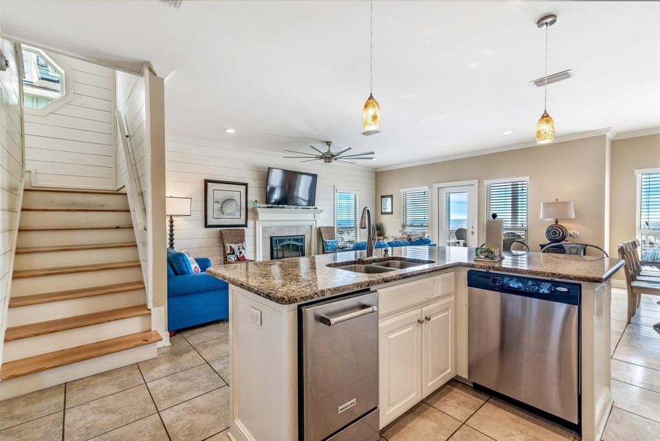 Kitchen island with granite counters, stainless steel dishwasher and sink, amber pendant lights overhead.