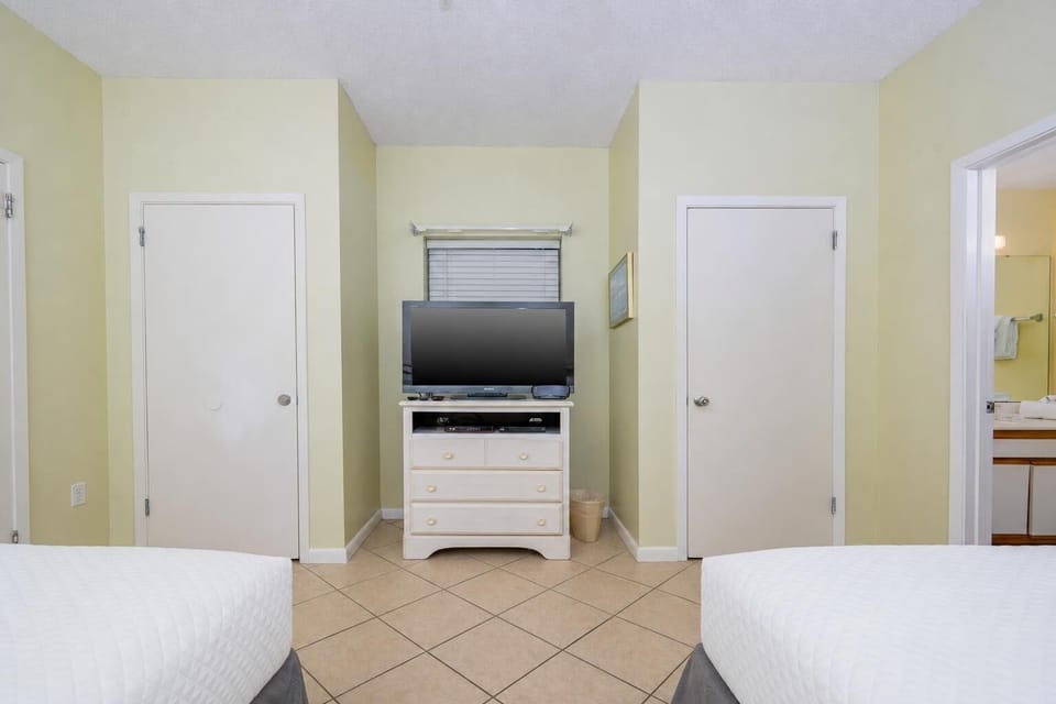 Brightly colored walls frame a cozy guest room featuring two double beds and a TV on a dresser, with a bathroom door visible