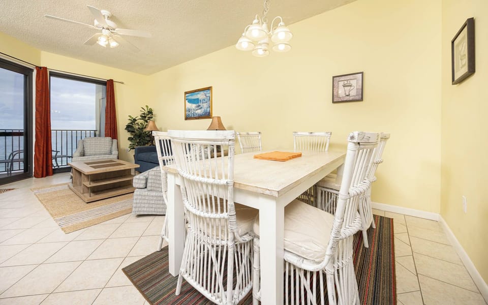 Dining area features a white table with six chairs, a cozy seating arrangement, and a view of the gulf through large windows