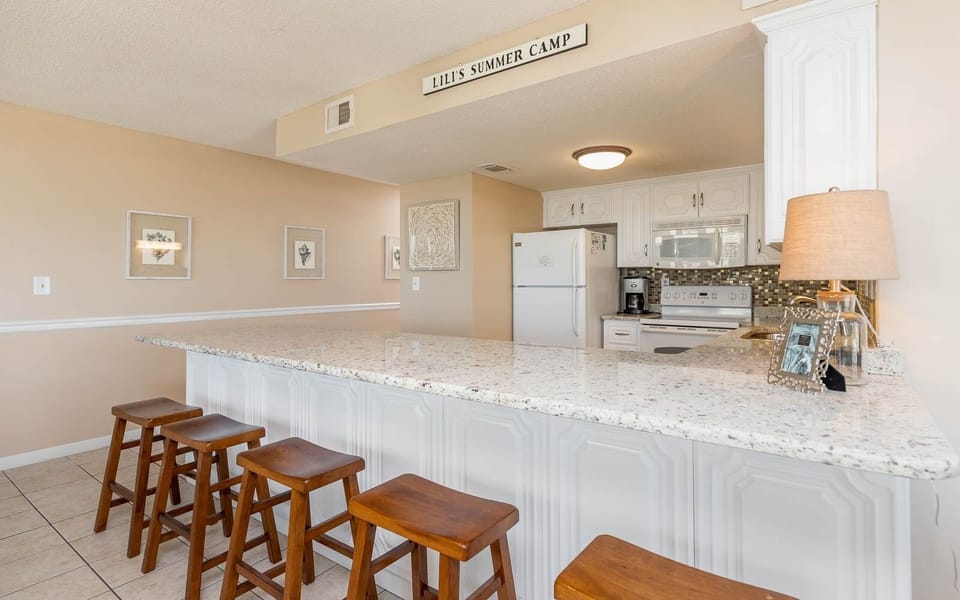 This kitchen features white cabinetry, granite countertops, and a breakfast bar with wooden stools for casual dining