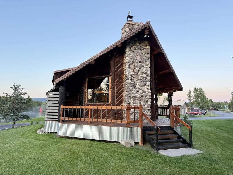 The cabin's exterior is a harmonious mix of natural materials, with large logs and weathered wood giving it an authentic, mountain cabin feel.