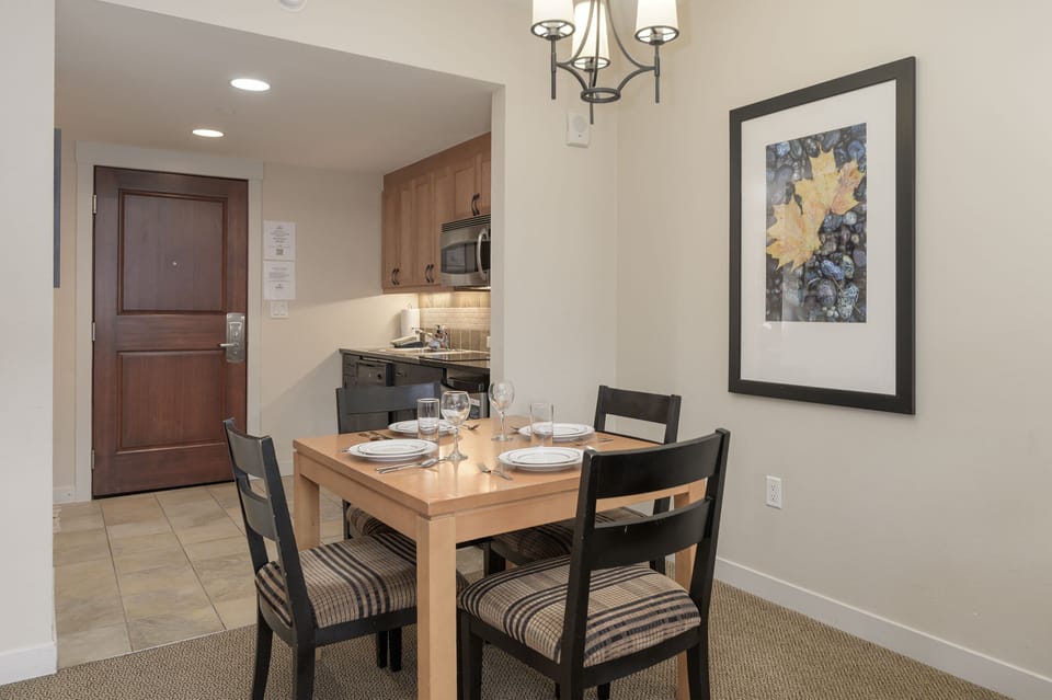 - Inviting dining space set for four with soft cushions and warm wood table - Overhead chandelier lighting creates a relaxed atmosphere for mealtime - Open layout leads into a fully equipped kitchen with stainless appliances
