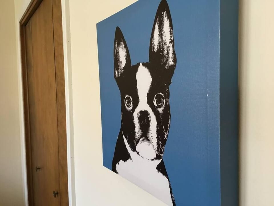 Black and white dog artwork on a blue canvas hangs beside a wooden door in the hallway.