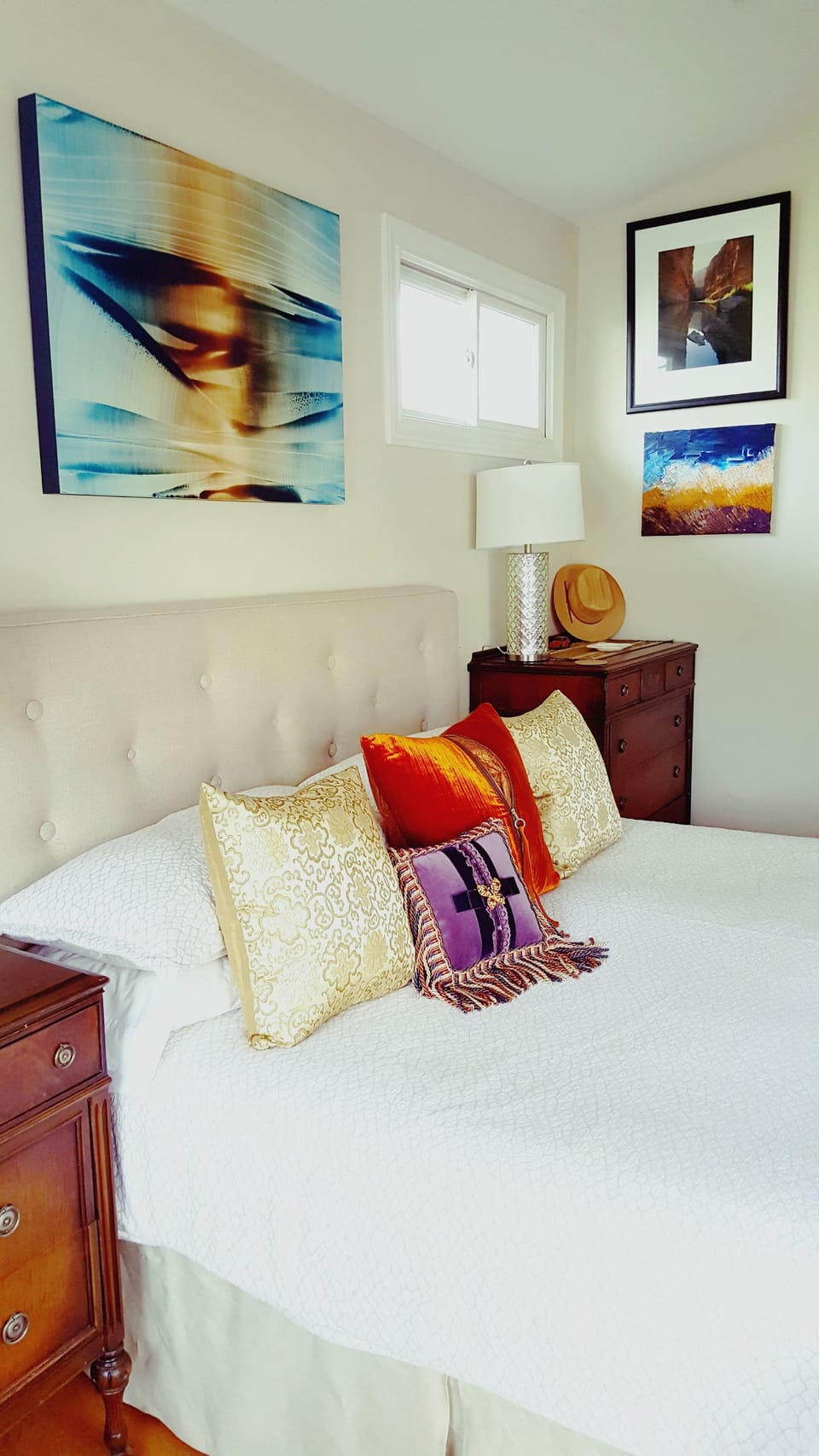 King bed between antique bureaus with modern lamps. Art by painter Roi James.