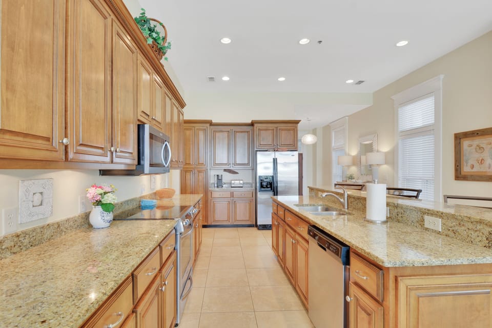 Galley Kitchen with Granite Counters - Long kitchen layout includes stainless appliances, wood cabinetry, tile backsplash, and counter space for meals or takeout.