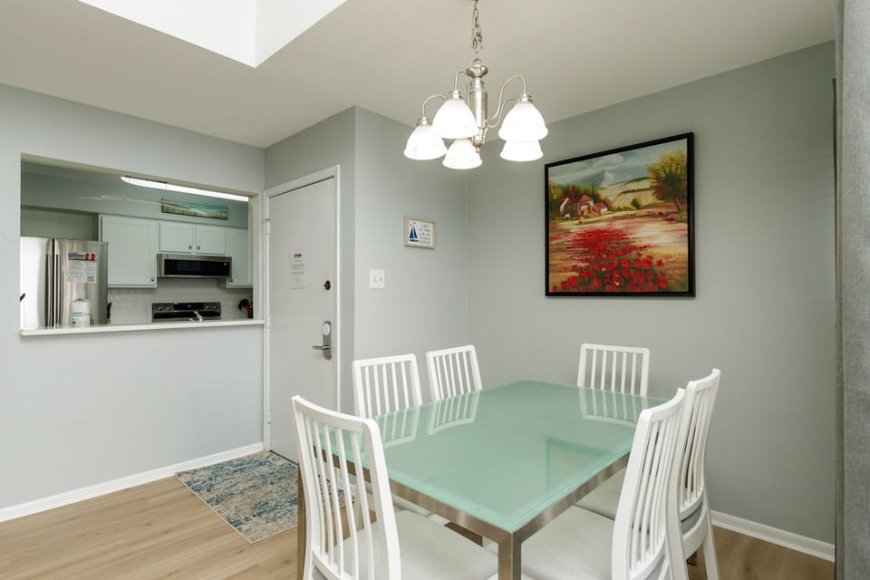 Your bright dining space features a glass-top table for six, perfect for family meals under the elegant chandelier.