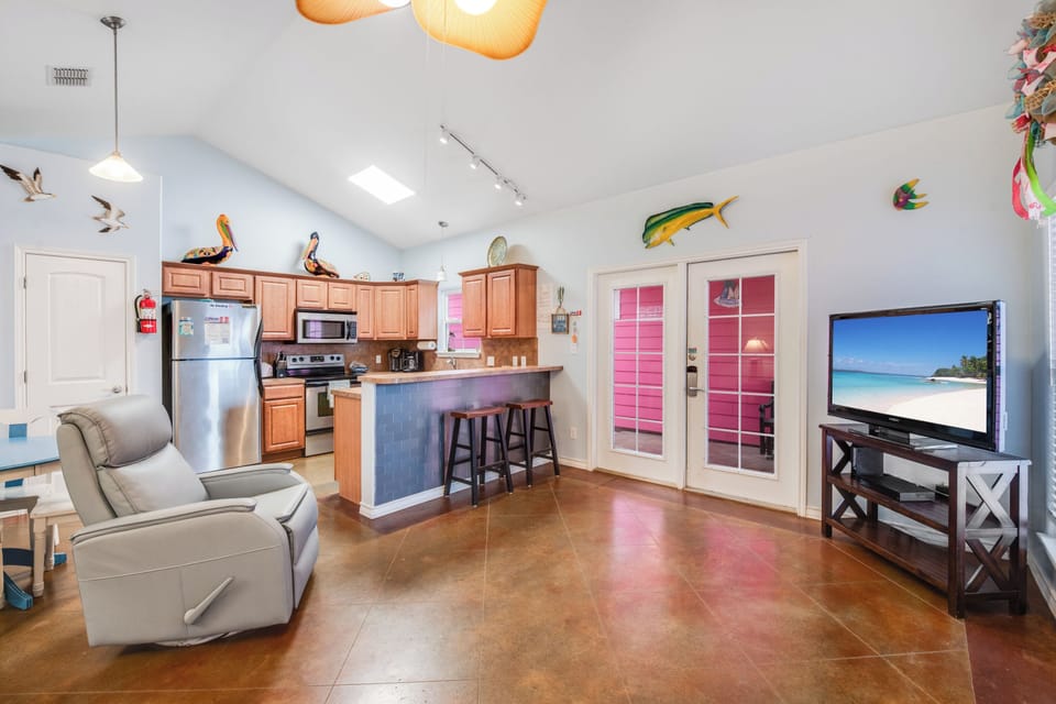 Relax in your bright, open-concept space where a fully equipped kitchen flows seamlessly into your comfortable living area with tropical beach scenes on the TV.