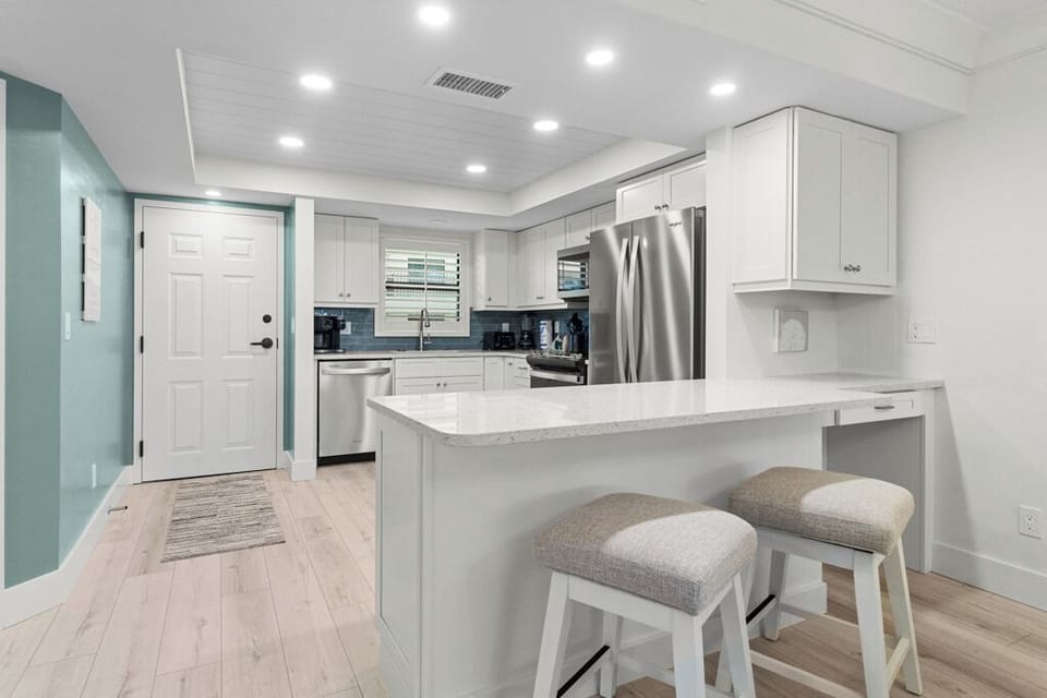 Bright coastal kitchen with white cabinetry, stainless steel appliances, and a sleek blue tile backsplash.