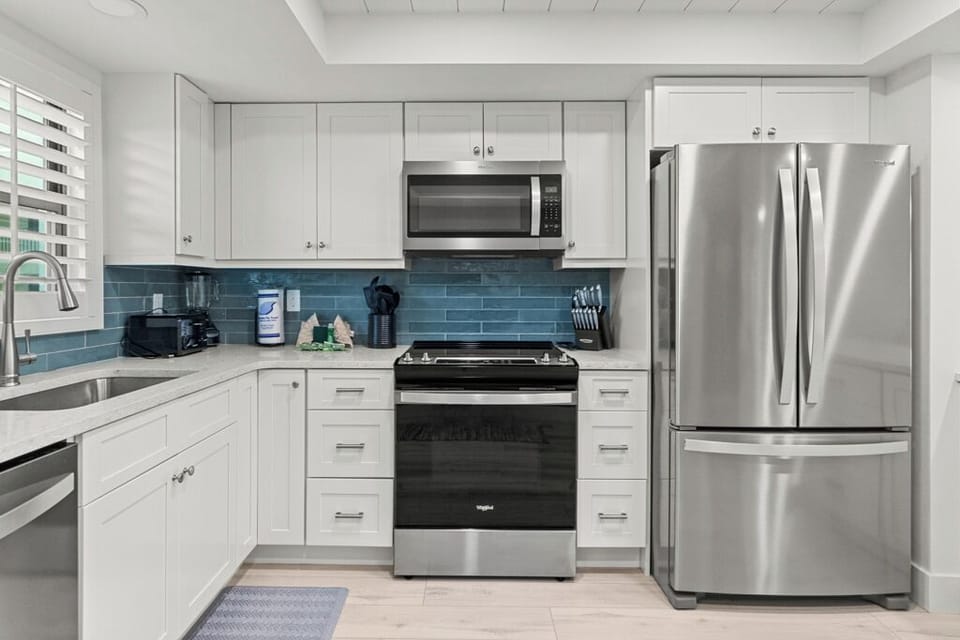 Bright coastal kitchen with white cabinetry, stainless steel appliances, and a sleek blue tile backsplash.