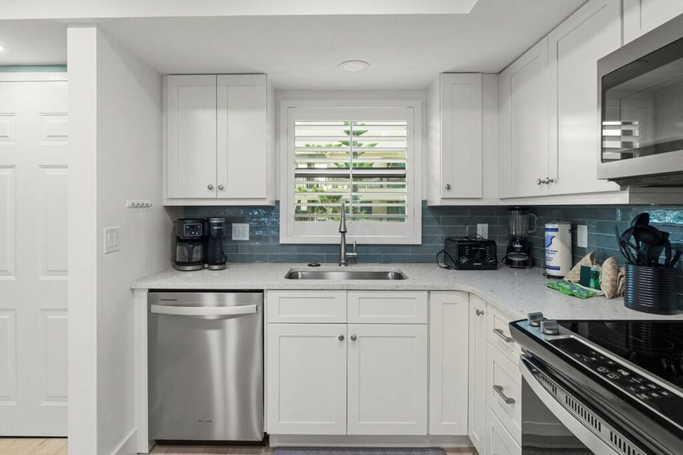 Bright coastal kitchen with white cabinetry, stainless steel appliances, and a sleek blue tile backsplash.