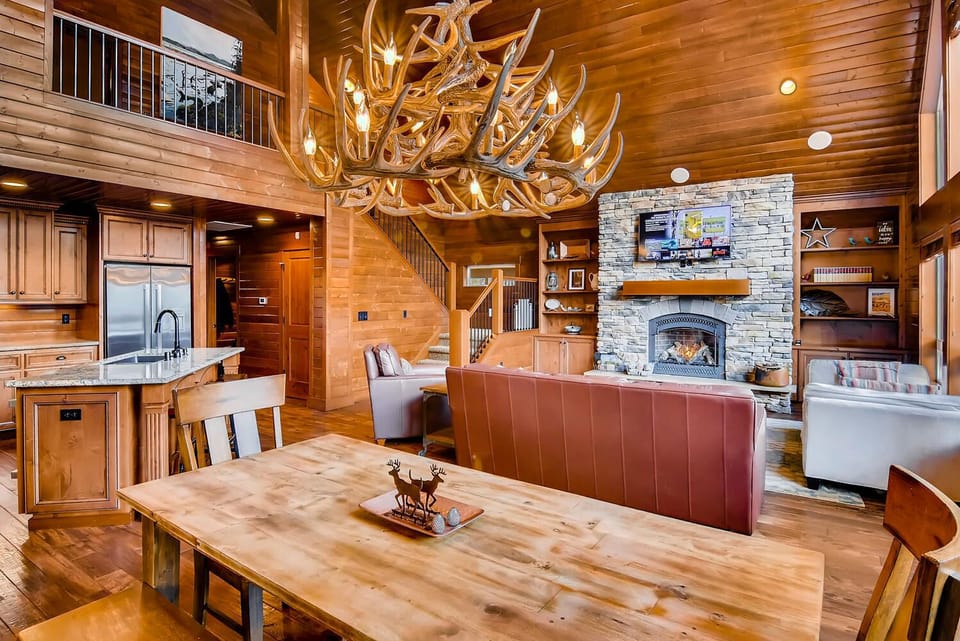 Crestview - Vacation Rental 365 - Grand lodge-style dining area with antler chandelier and open concept stone gas fireplace, and vaulted cedar walls