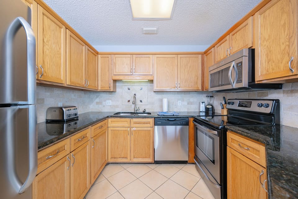 Kitchen features wooden cabinetry, granite countertops, and a breakfast bar with seating, leading to a cozy living area