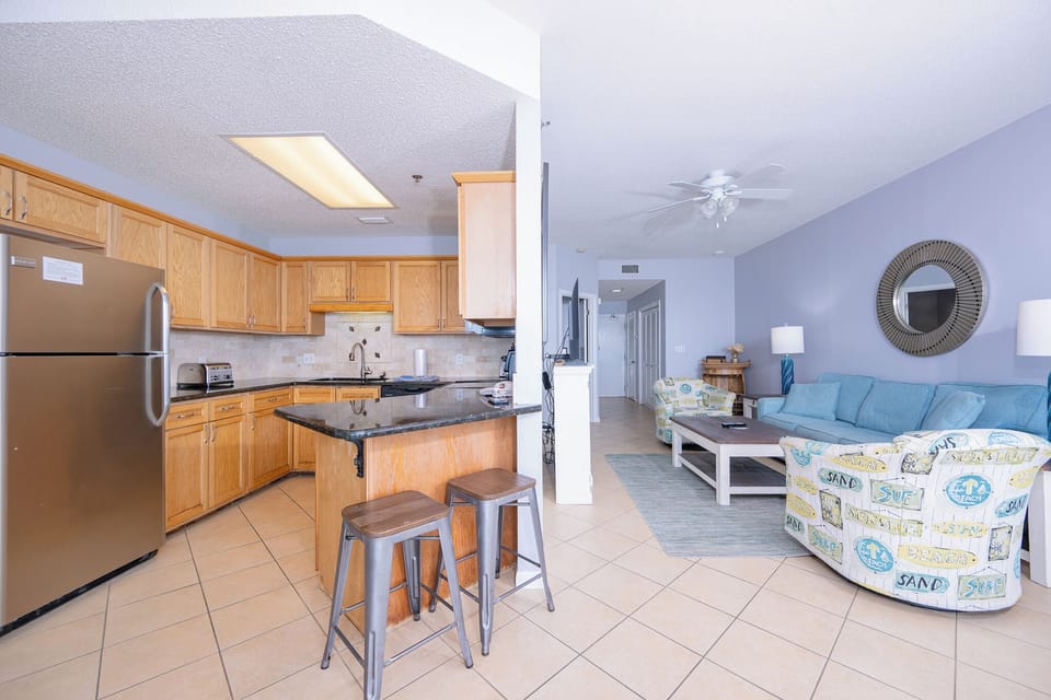 The modern kitchen features wooden cabinetry, a sleek black refrigerator, and a breakfast bar with stylish metal stools