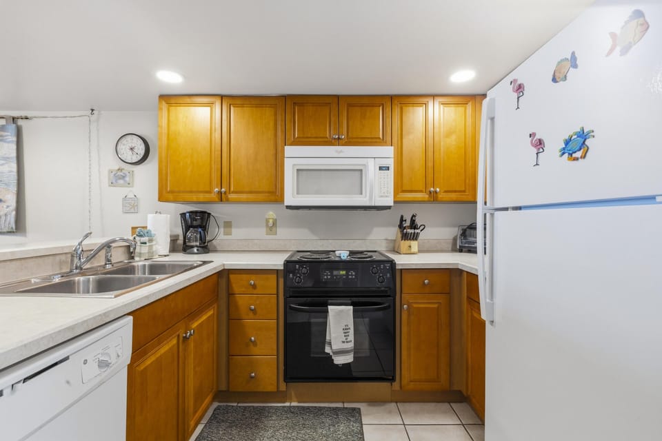U-shaped kitchen with honey oak cabinets, black stove, white microwave, and double stainless steel sink.