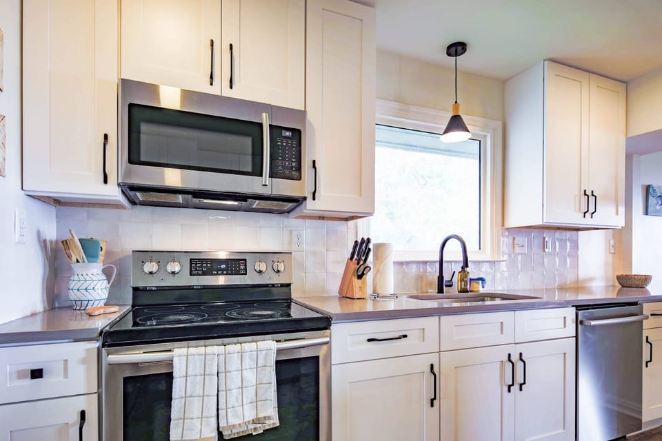 The newly renovated kitchen features stainless steel appliances, white cabinetry and a tiled backsplash.