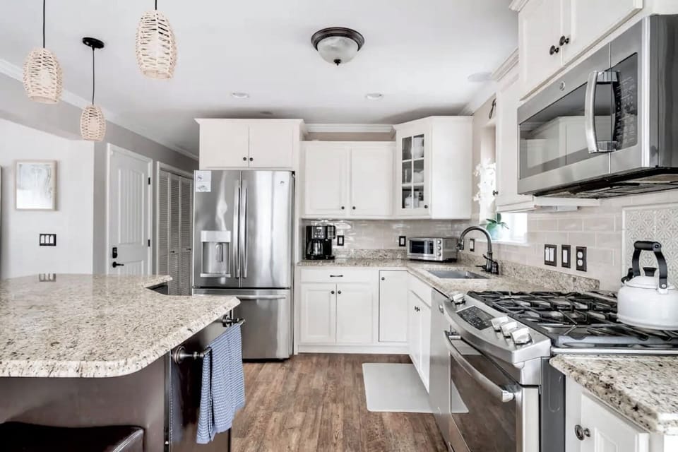 Cook with ease in this bright, modern kitchen featuring stainless steel appliances, granite countertops, and an island. White cabinetry and stylish pendant lighting create a clean, inviting space perfect for preparing any meal.