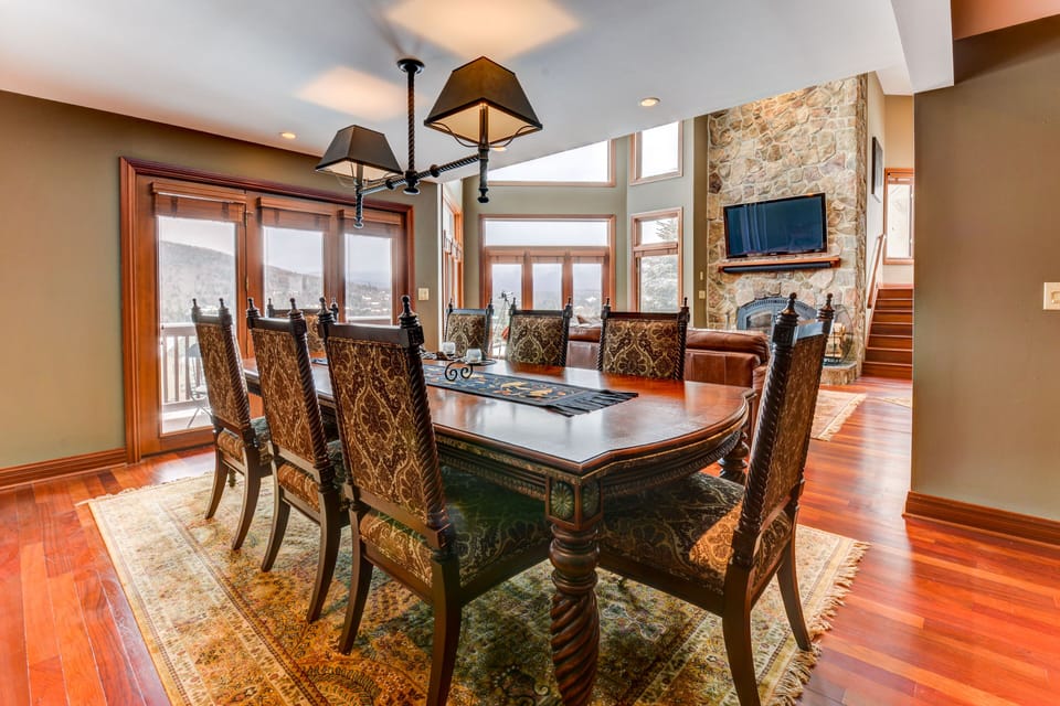 The living/dining area features a beautiful, open-concept space with a luxurious dining table for 8 and a cozy seating area surrounding a massive stone wood-burning fireplace.
