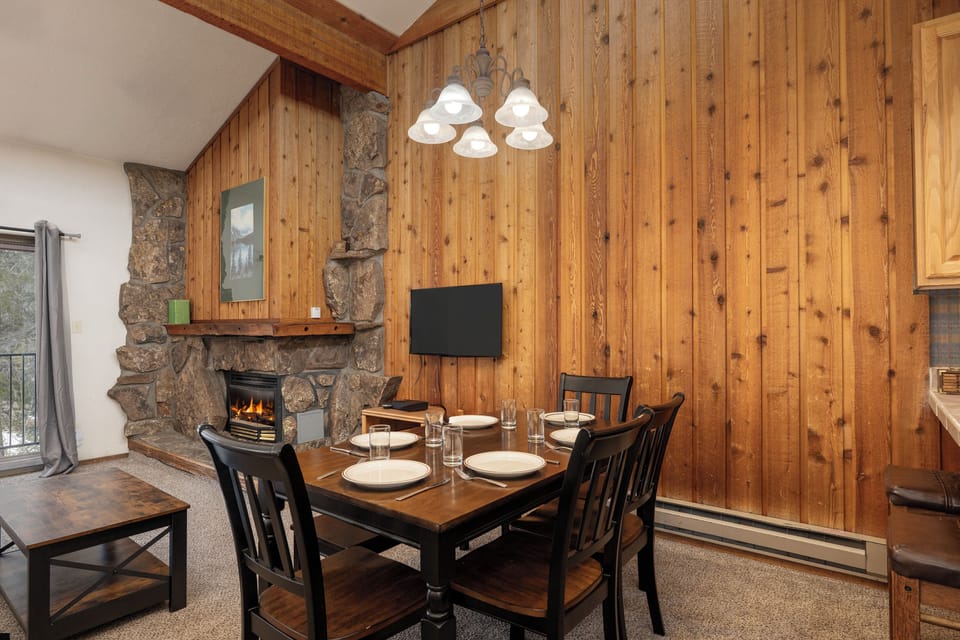 Cozy dining space with warm wood paneling, stone fireplace, and intimate table setting creates your perfect mountain retreat atmosphere.