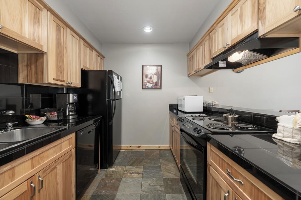 Prepare your favorite meals in this fully equipped galley kitchen featuring warm wood cabinetry, black granite counters, and all essential appliances.