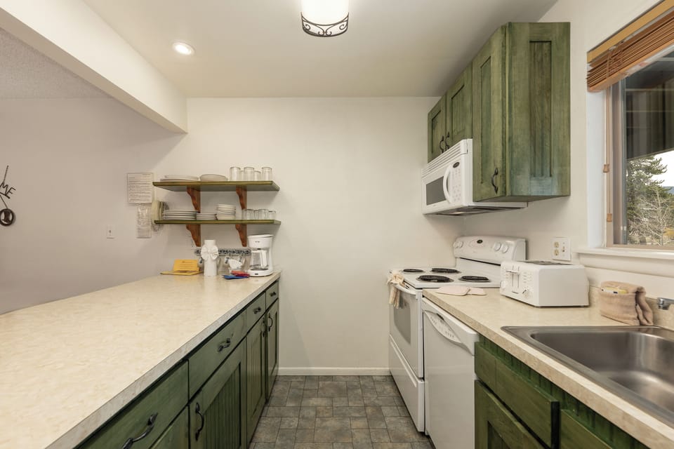 Prepare your favorite meals in this charming galley kitchen with rustic green cabinets, modern appliances, and ample counter space for cooking adventures.