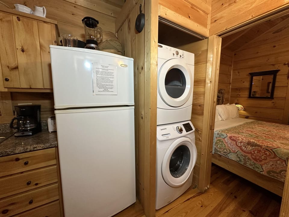 Stacked washer and dryer tucked into a natural wood nook between the kitchen and bedroom with patterned bedding.