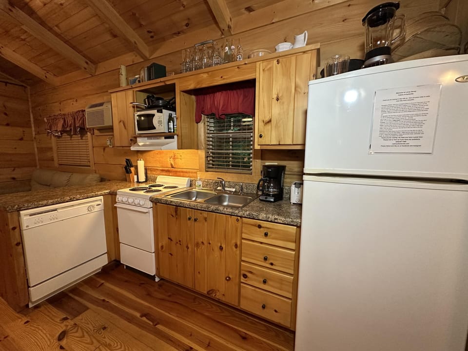 Kitchen with natural wood cabinets, granite countertops, white appliances, and a window with red valance.
