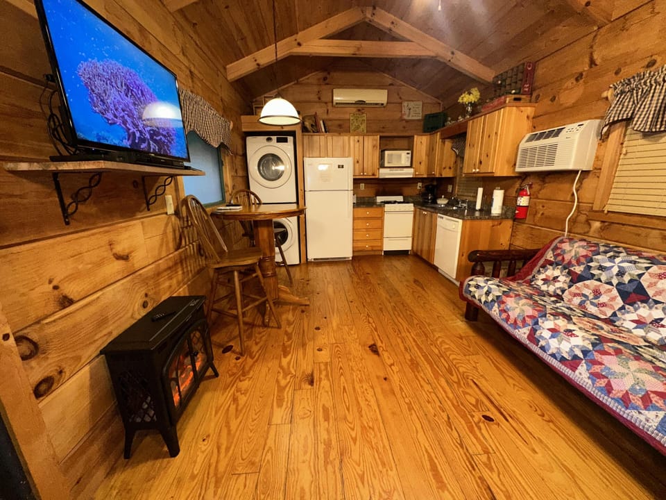 Wood-paneled living area with stacked washer and dryer, round wooden table, and floral quilt on futon couch.