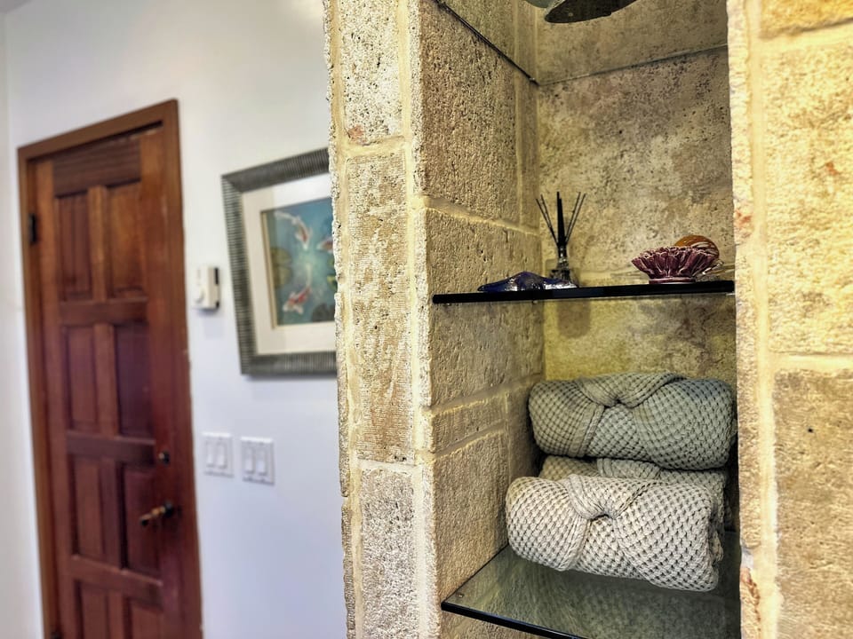- Step into serenity with soft spa towels neatly arranged on sleek glass shelves
- Fragrant reed diffuser and coastal décor set a soothing, elegant tone
- Earthy stone textures and warm wood accents invite you to unwind in style
