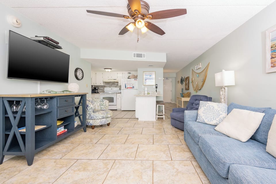 The living area features a large TV, comfortable seating, and a view into the bright kitchen, perfect for relaxation