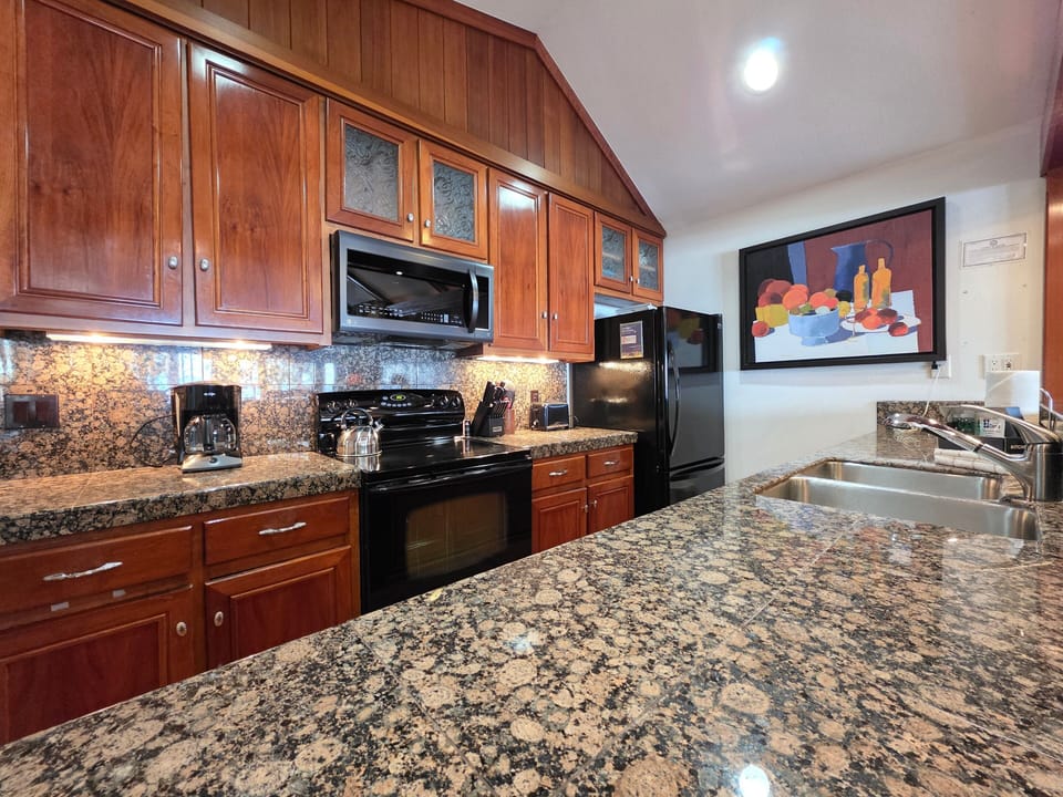 Kitchen with sink, range, microwave, coffee maker, refrigerator, mirror, cabinets, counters, and hallway opening.