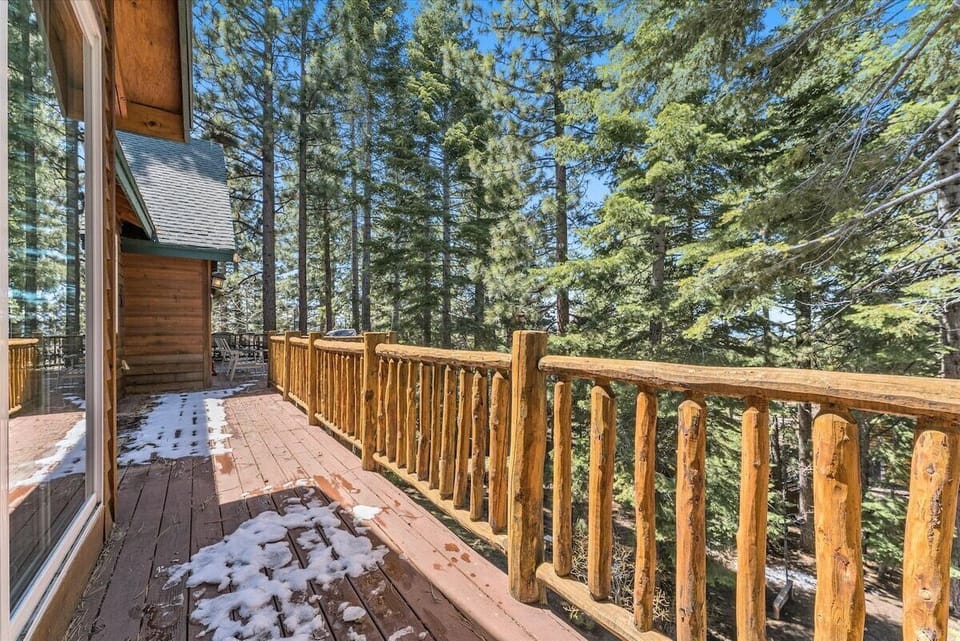 Back deck with patio table seating, railing, snow patches, trees, and exterior wall.