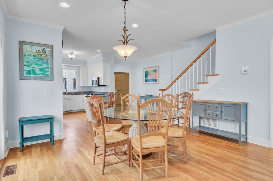 Gather around your elegant dining table with warm wood floors, charming coastal artwork, and open kitchen access for memorable meals.
