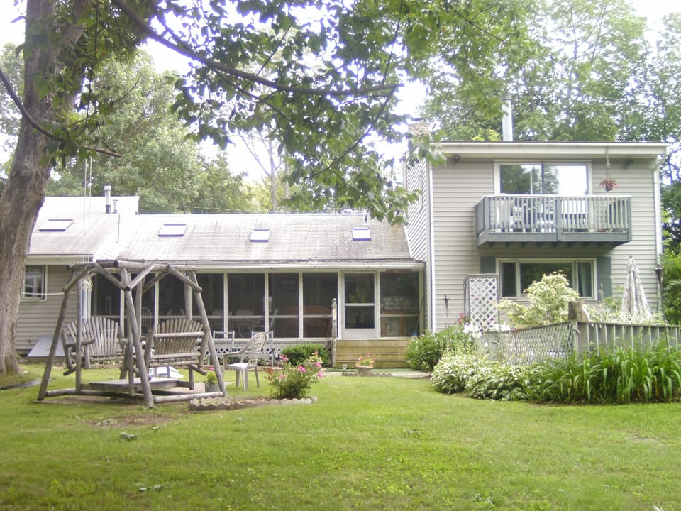 Back of house with double cedar swing, screen porch, gas grill and eating area.