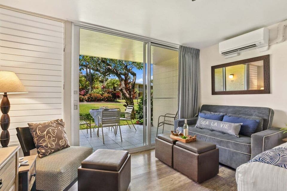 A bright, airy living area featuring a comfortable sofa, cooling AC, and a direct view of the greenery.