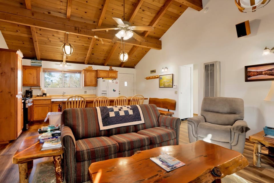 Cozy mountain living room with wood ceilings, stone fireplace, comfy seating, and smart TV—perfect for relaxing evenings, movie nights, and warm cabin vibes after outdoor adventures.