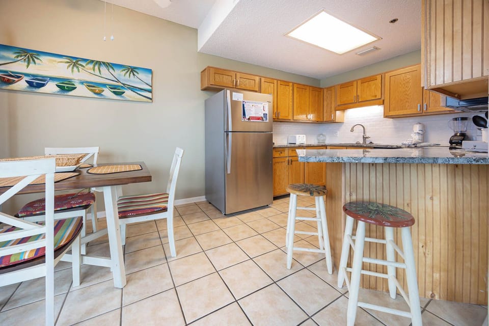 Kitchen area with wooden cabinets, granite countertops, and a cozy dining table featuring colorful cushioned seating