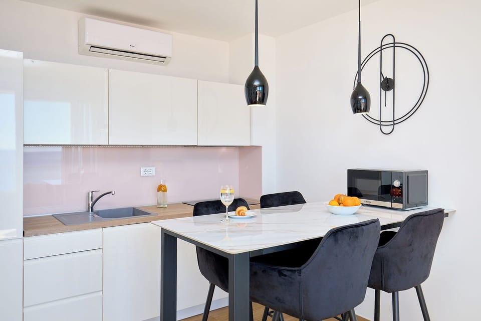 Enjoy meals in a chic dining area with a marble-top table and plush velvet chairs, set against a sleek, fully-equipped kitchenette.
