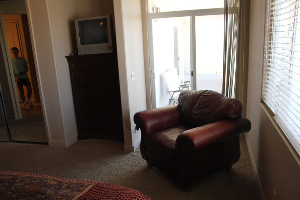 TV and oversized chair by door to balcony off of the master bedroom with king be