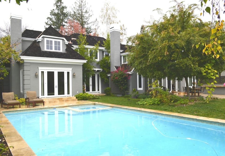 Backyard swimming pool surrounded by lush green trees.