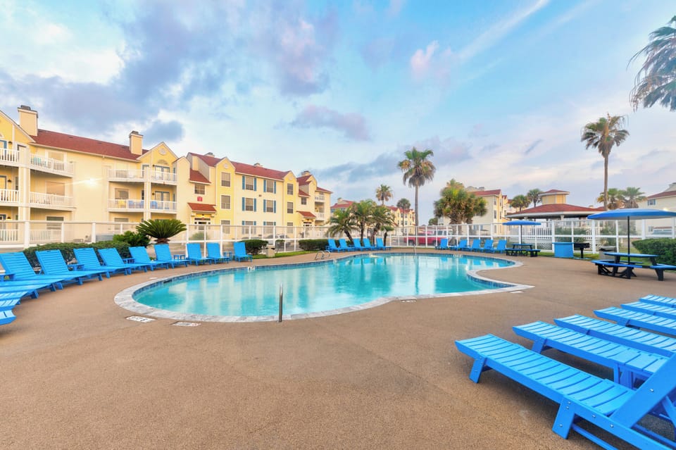 Tropical resort featuring swimming pools surrounded by palm trees and colorful buildings under bright blue skies.
