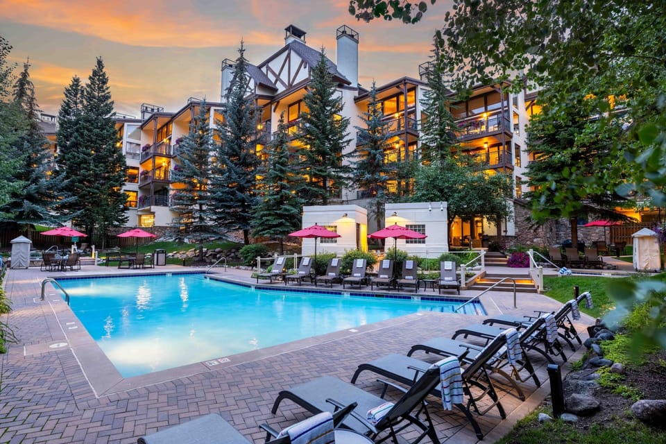 Mountain resort property with outdoor pool and seasonal amenities, nestled among evergreens beneath a vibrant evening sky.
