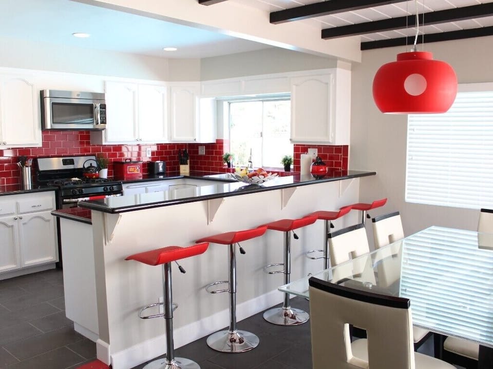 - Modern kitchen with sleek white cabinets and bold red backsplash design   - Stylish bar seating with red stools perfect for casual dining or entertaining   - Bright open layout with modern lighting and stainless steel appliances