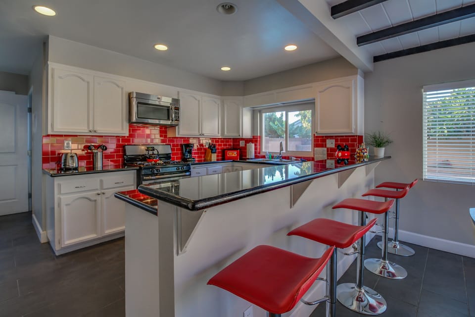 - Kitchen with sleek black countertops and bright red backsplash   - Row of modern red bar stools perfect for casual dining   - Open layout making cooking and entertaining easy and fun