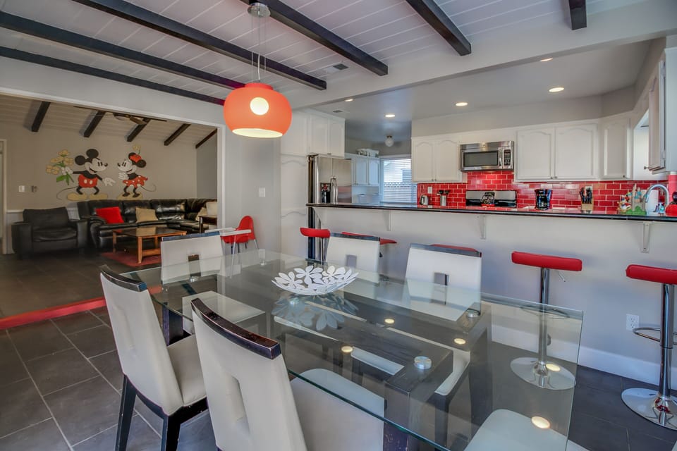 - Spacious dining and kitchen area designed for group gatherings   - Glass dining table and red bar stools creating a modern look   - Open concept layout with stylish lighting and vibrant accents