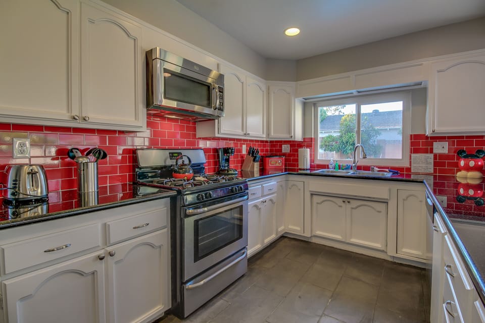 - Contemporary kitchen with stainless steel appliances for easy meals   - Red backsplash accents creating a modern and vibrant cooking space   - Functional layout with spacious countertops and storage for families